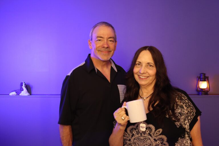 Donna and Terry from Rebuild With Clarity smiling together as Donna holds a warm white mug of tea